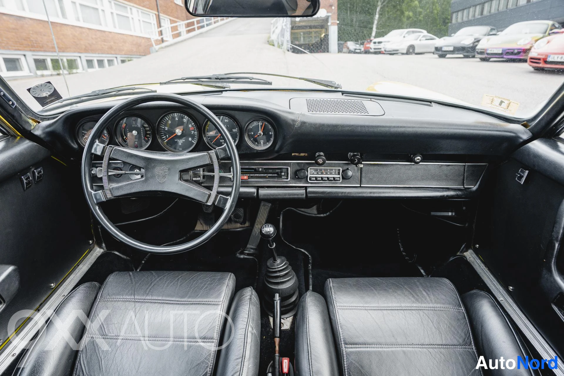 Yksityiskohta: Musta ohjaamo suoraan edestä: viisimittarinen kojelauta, Porsche-ohjauspyörä, vanha radio, viisivaihteinen vaihtajan kuppi ja kaksi mustaa istuinta.