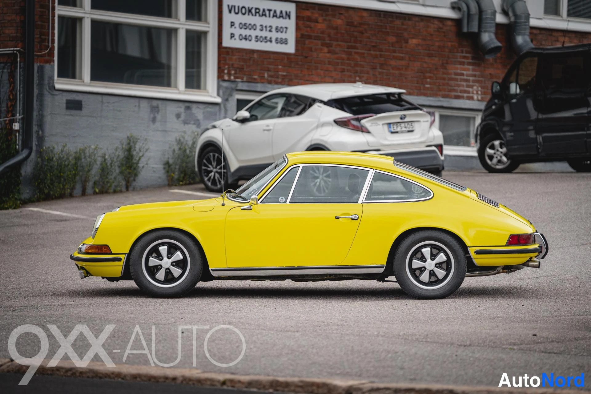 Sivulta: Keltainen klassinen Porsche-urheiluauto sivuprofiilista kuvattuna, vasen kylki näkyvissä parkkipaikalla talon vieressä.
