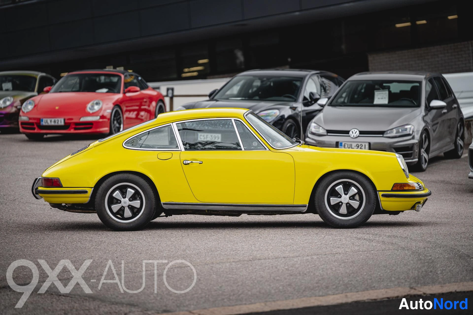 Takaviisto: Keltainen klassinen Porsche-urheiluauto takaviistokuvassa, takaosa ja vasen kylki näkyvissä paikoitushallissa muiden autojen seassa.