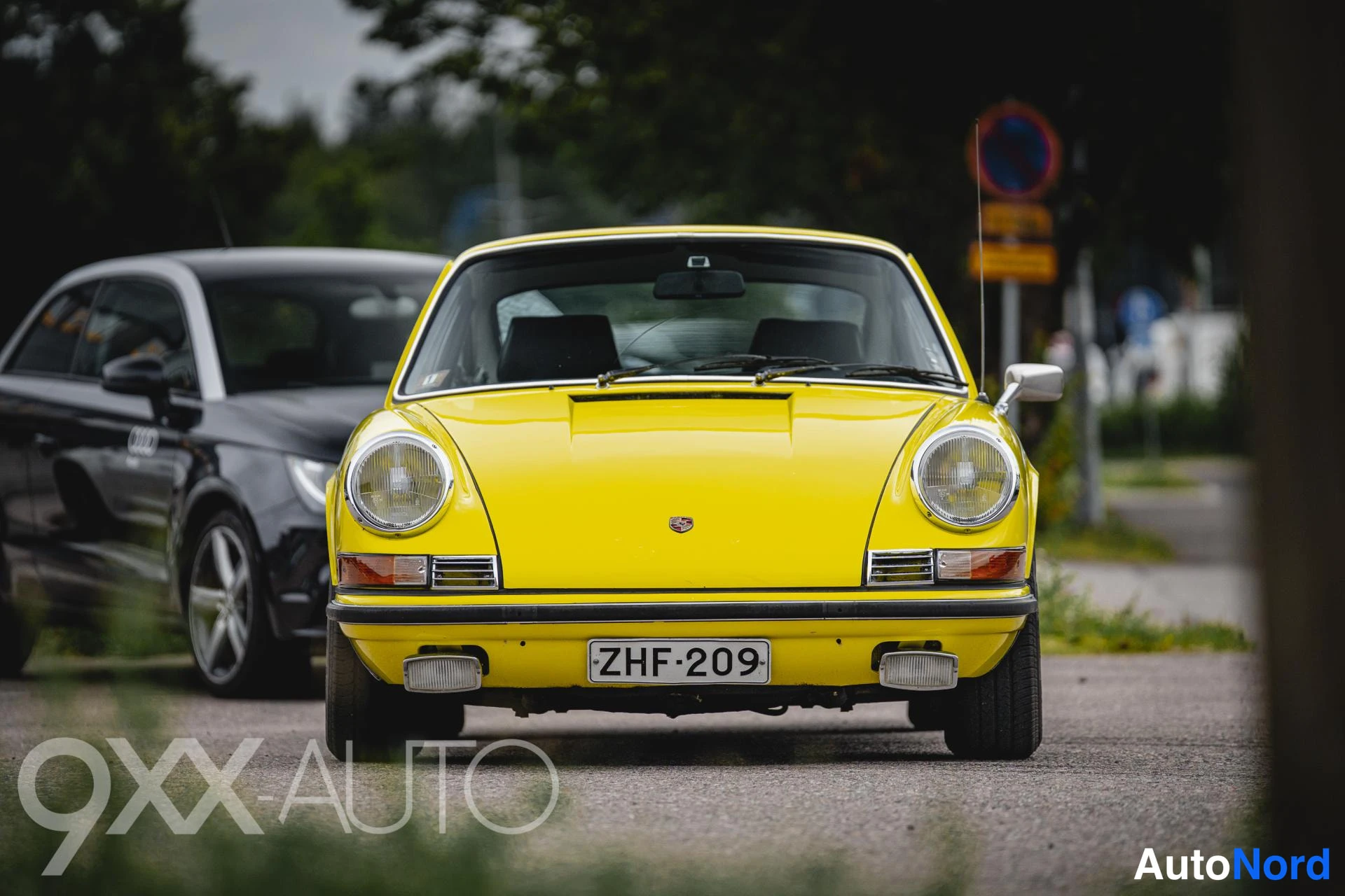 Edestä: Keltainen klassisen Porsche 911:n keula suoraan edestäpäin; pyöreät ajovalot, etupuskuri ja rekisterikilpi näkyvät.