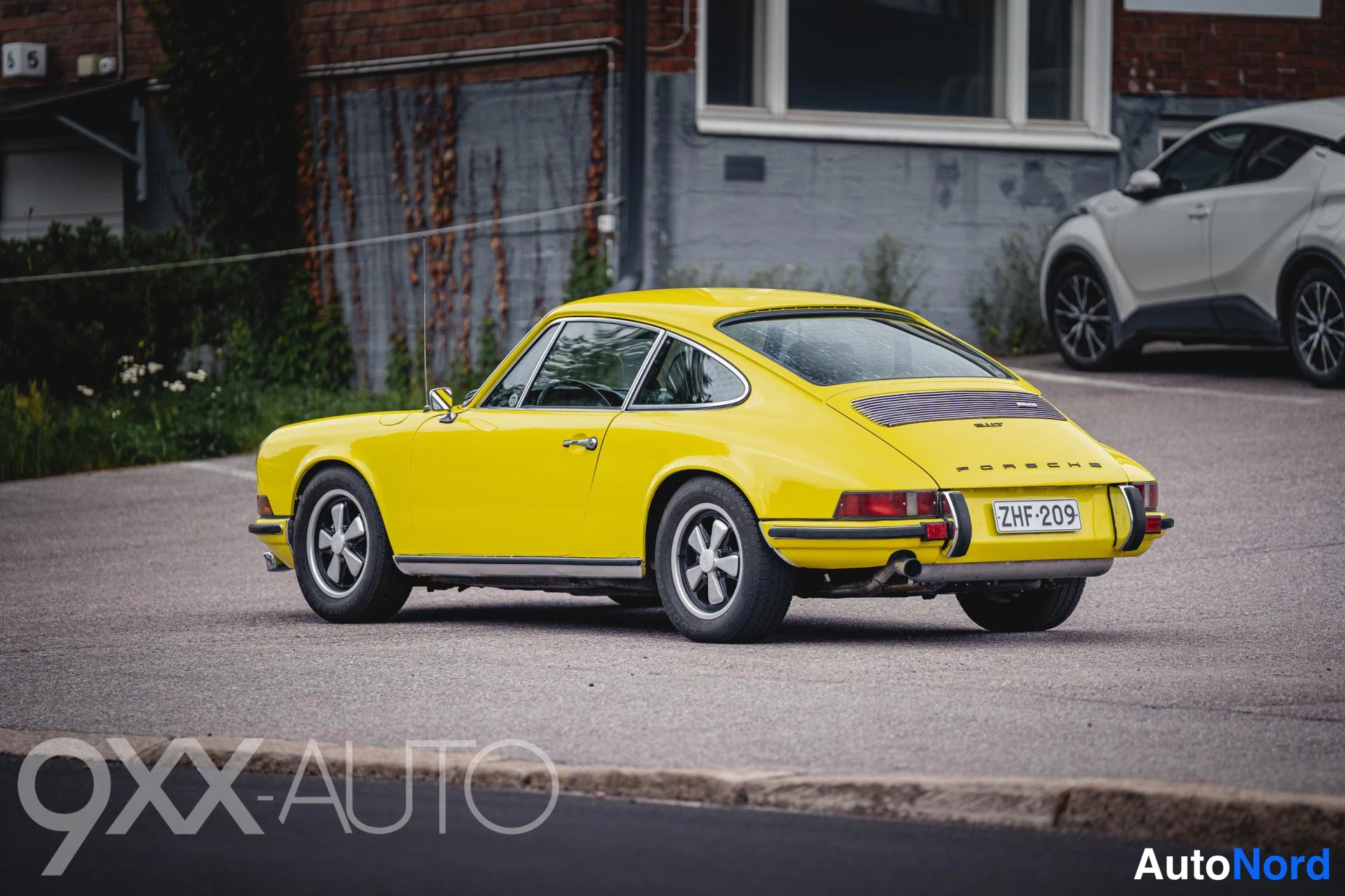 Takaviisto: Keltainen Porsche 911 -coupe takaviistosta oikealta; takamoottorin tuuletusritilä, Porsche-teksti, -kilpi ja peltivanteet näkyvät tieltä otetussa kuvassa.