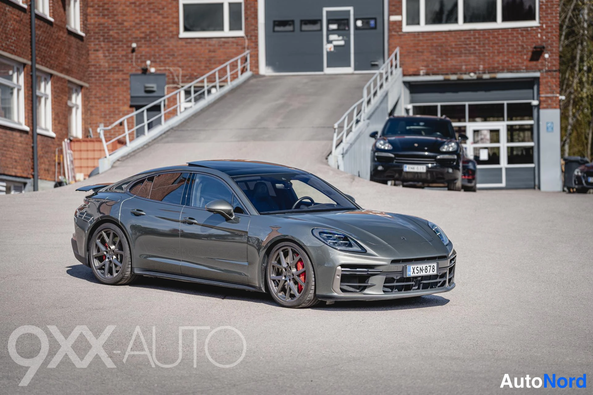 Etuviisto, nokka oikealle: Tummanharmaa Porsche Panamera etuviistosta oikealta, punaiset jarrusatulat ja rekisteri näkyvissä.