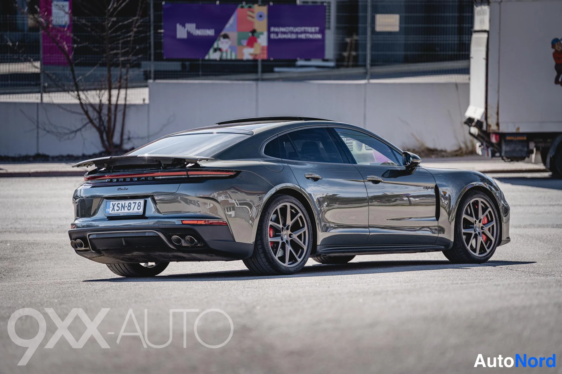 Takaviisto: Tummanharmaa Porsche Panamera takaviistosta vasemmalta, panoramic-katto ja kevytmetallivanteet näkyvissä.
