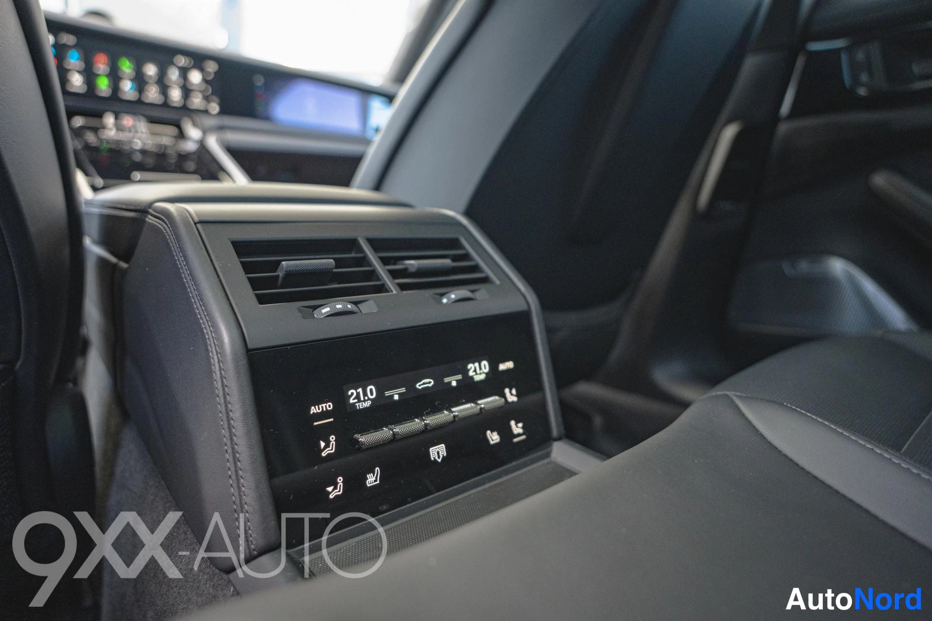 Muu: Takaistuinten välinen paneeli ilmastointiaukoilla ja kosketusnäytöllä, jossa lukee 21,0 ja AUTO.