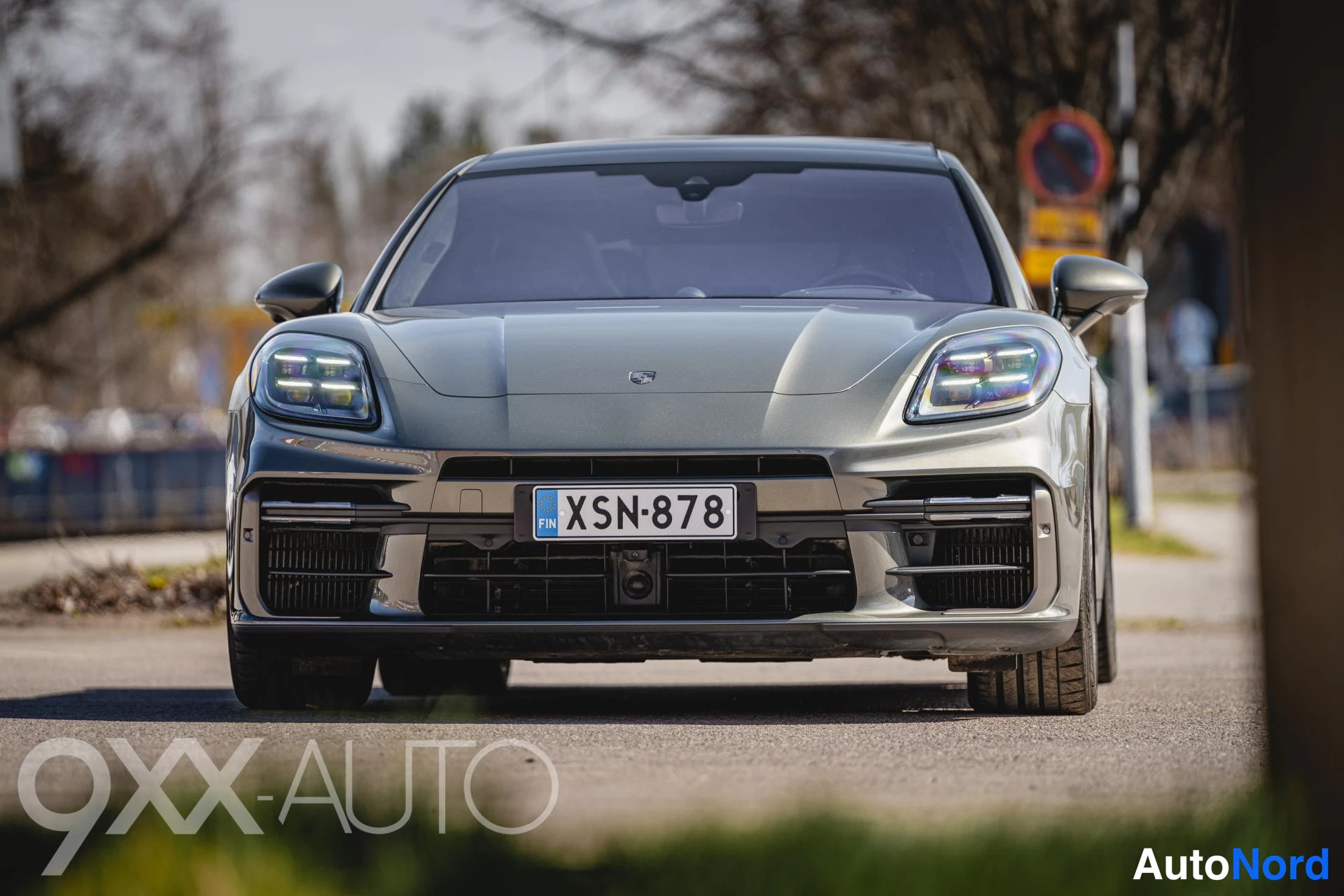 Edestä: Tummanharmaa Porsche Panamera suoraan edestä, rekisteri ja suuret ilmanottoaukot näkyvissä.