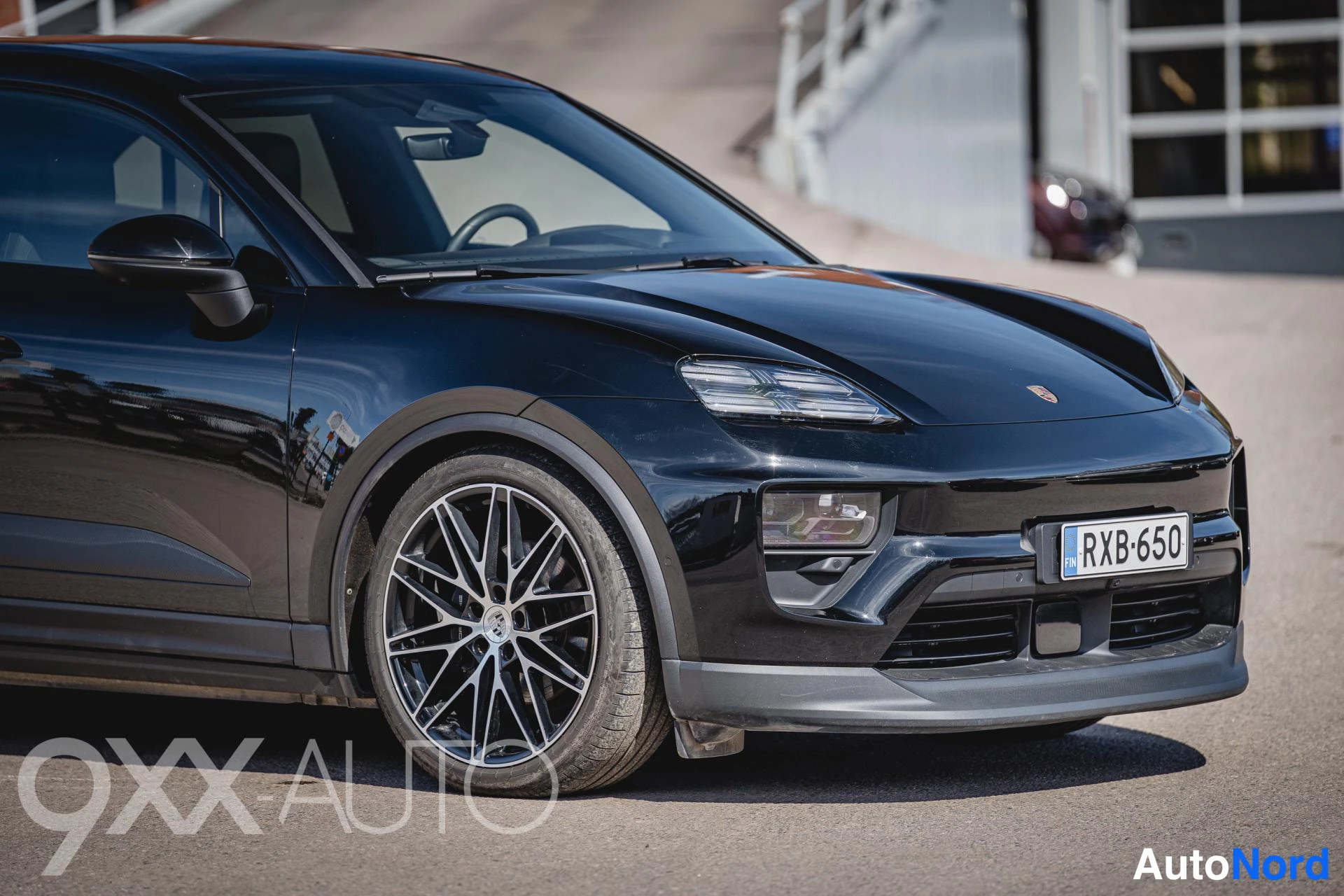Etuviisto, nokka vasemmalle: Musta Porsche Macan etuosa kolmella neljäsosalla, etusäleikkö ja rekisterikilpi näkyvät.