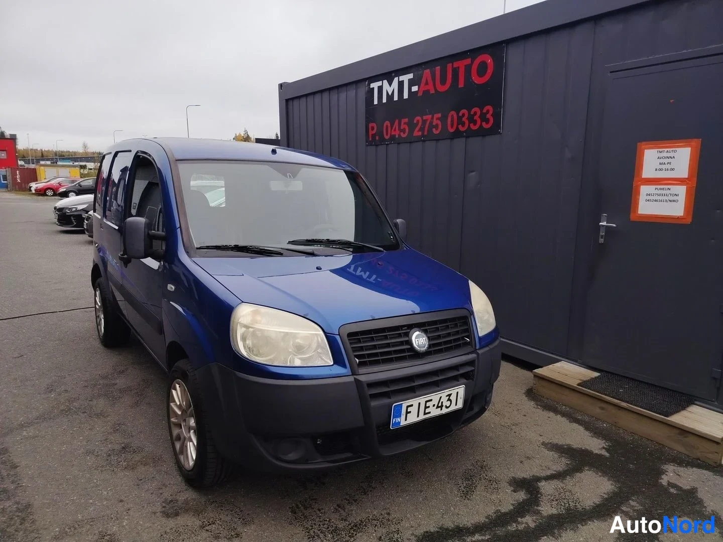 Etuviisto, nokka oikealle: Sininen Fiat Doblo etukulmasta oikealta, etusäleikössä Fiat-merkki, rekisteritunnus.