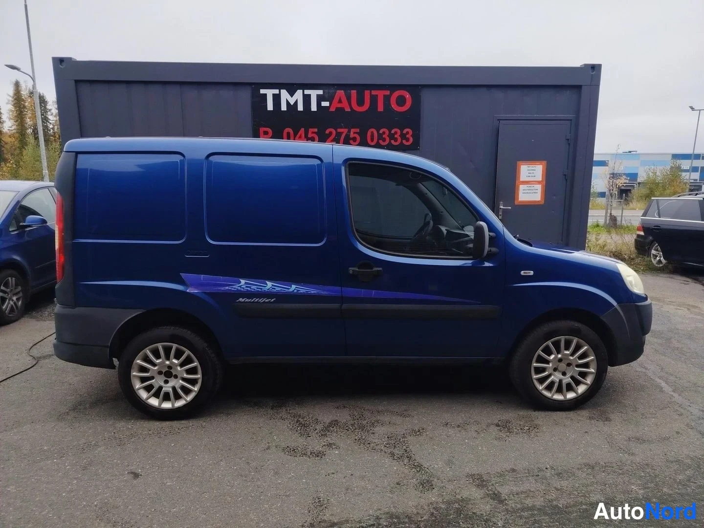 Etuviisto, nokka oikealle: Sininen pakettiauto sivulta etunosa oikealla, vaaleat vanteet.