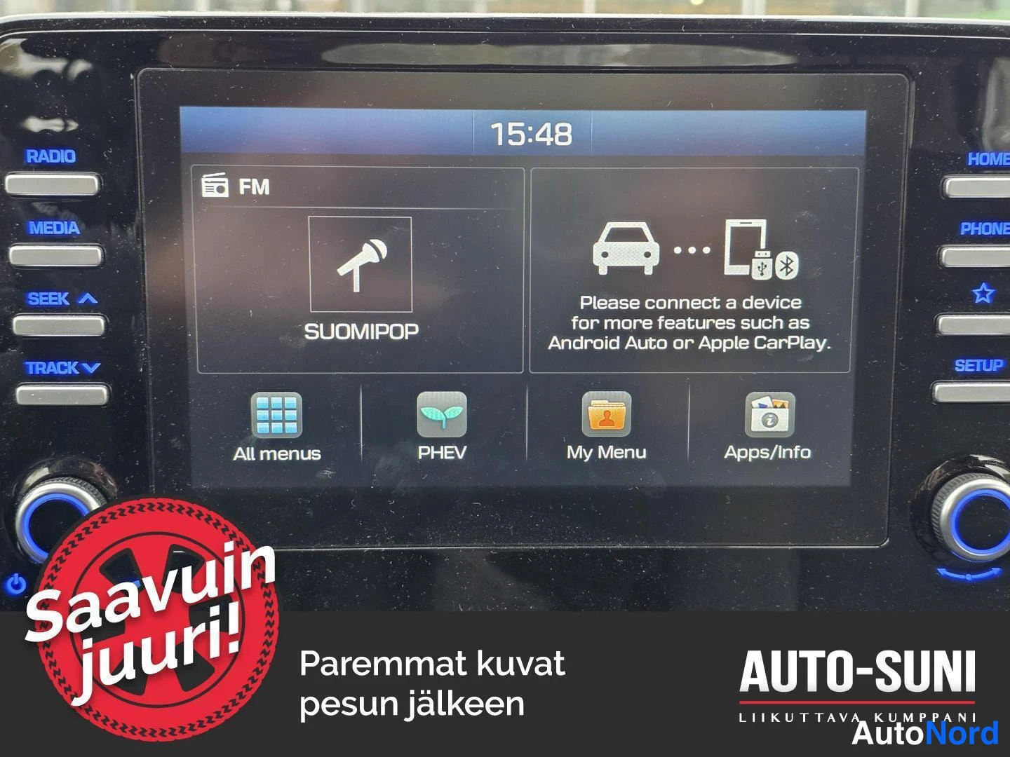 Muu: Kojelaudan infotainment-näyttö, jossa radio FM (SUOMIPOP), Aikaa 15:48 ja viesti 'Please connect a device for more features such as Android Auto or Apple CarPla