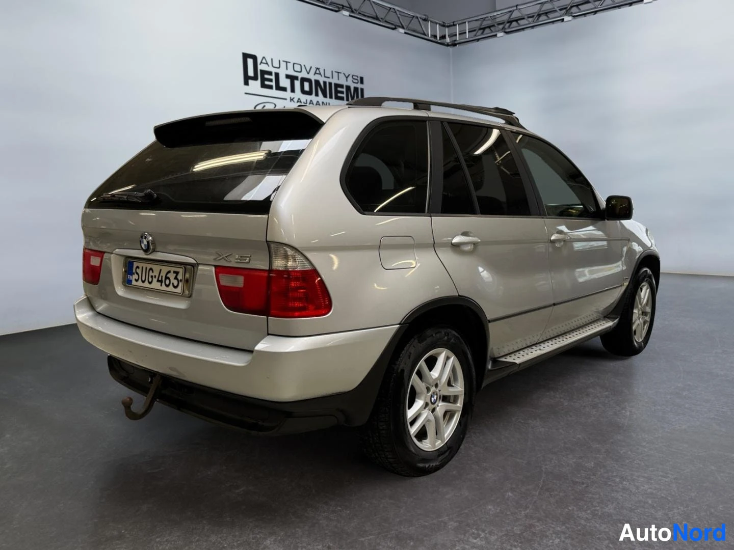 Takaviisto: BMW X5 takaviisto oikealta: hopea korikonepelti- ja takapaneelialueilla, rekisterikilpi, takavalot ja vetokoulu näkyvät.