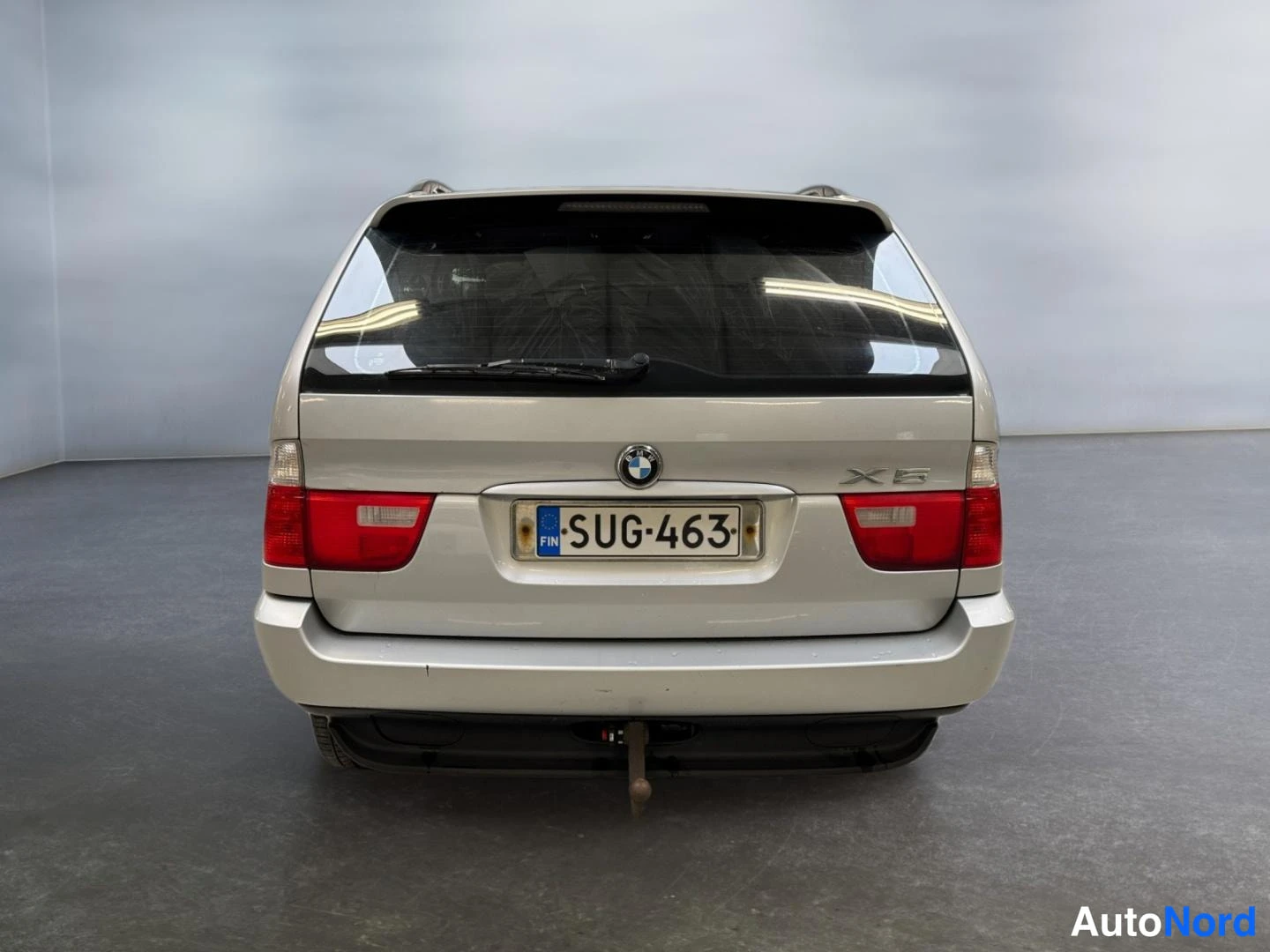Takaa: BMW X5 suora takaa: hopea takapaneeli, rekisterikilpi, punaiset takavalot, takalasinpyyhkijä ja vetokoulu näkyvät.