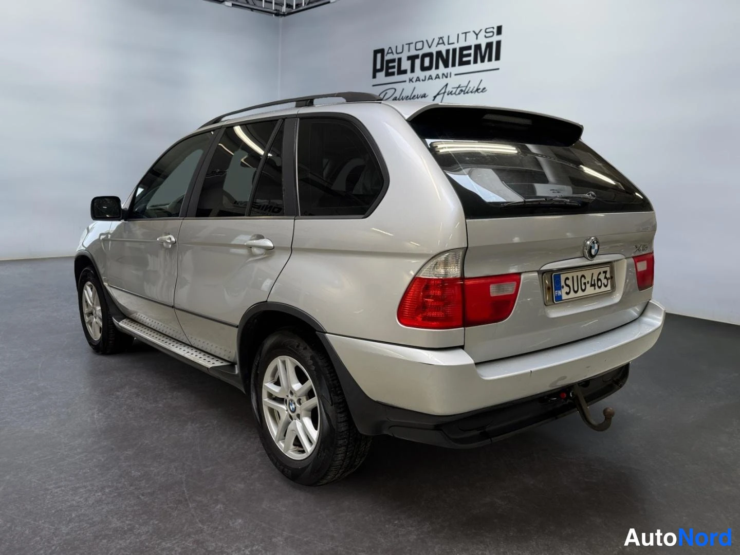 Takaviisto: BMW X5 takaviisto vasemmalta: hopea koripaneelit, rekisterikilpi, punaiset takavalot, kattokaiteet ja sivulankut näkyvät.
