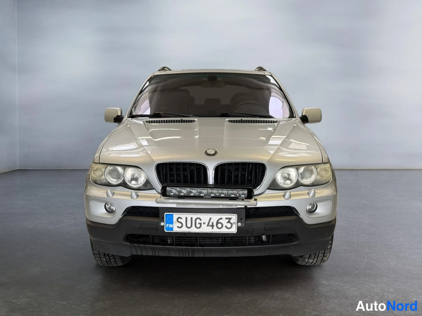 Edestä: Suora etukuva hopeanvärisestä BMW X5:stä; rekisterikilpi ja lisävalo tangon päällä.