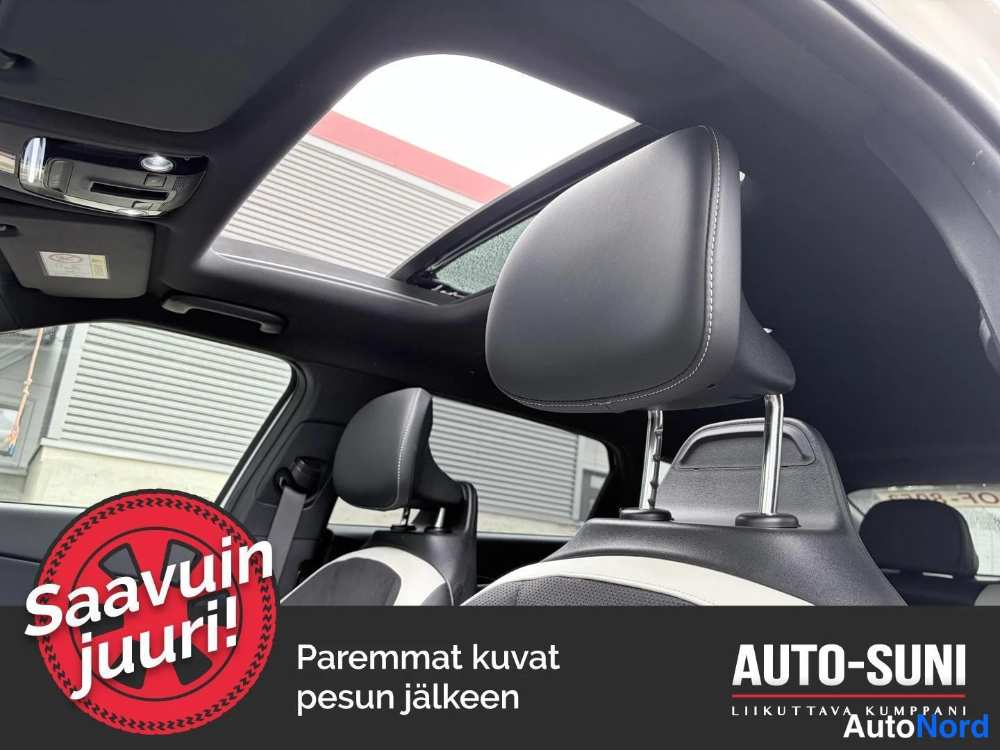 Ohjaamo: Interior view of two front seats with white leather bolsters and black headrests, featuring a large sunroof above that lets in daylight.