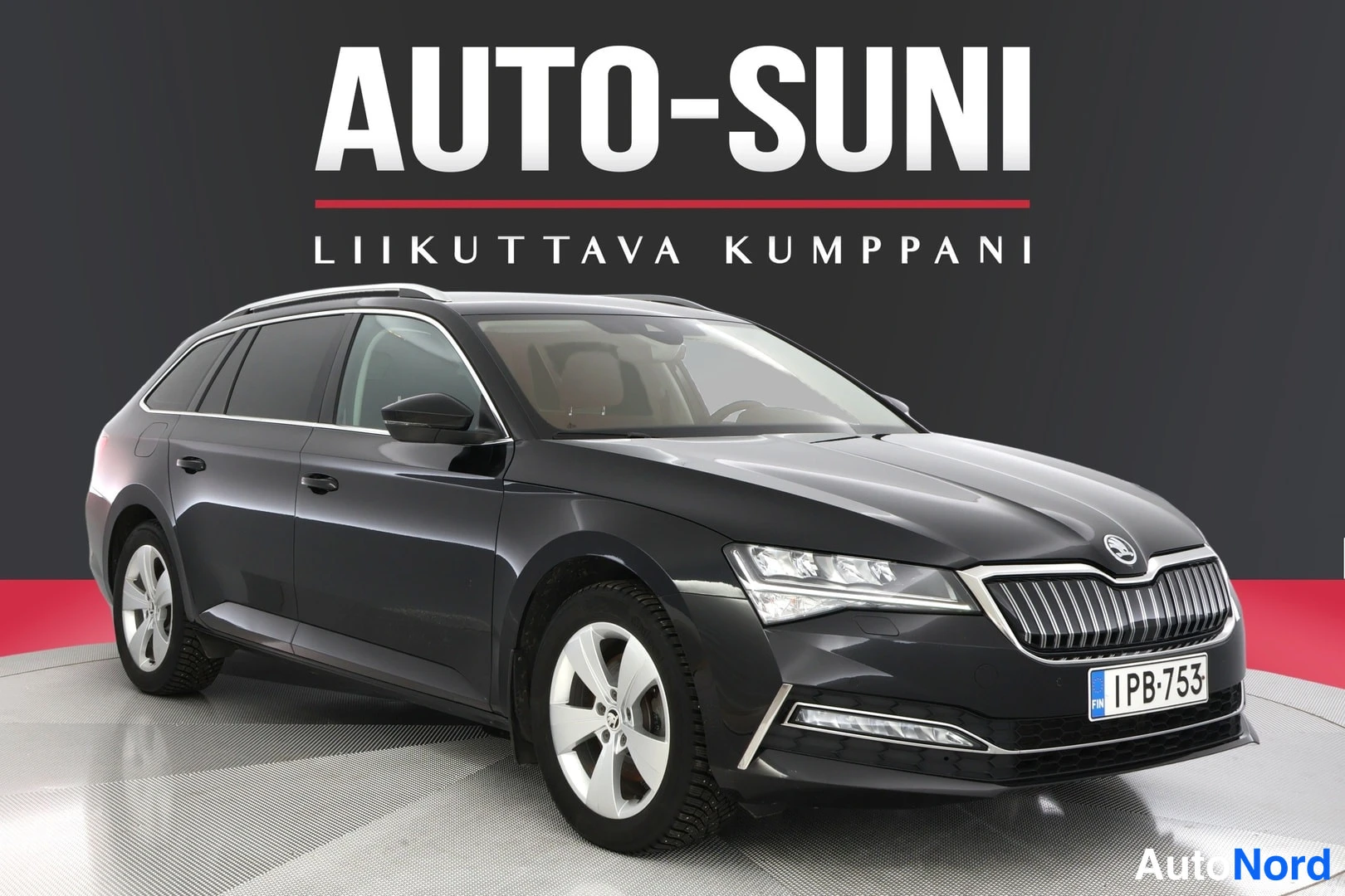 Etuviisto, nokka vasemmalle: Front three-quarter view of a dark grey Skoda Superb station wagon from the front-left angle. Visible features include LED headlights with DRLs, roof r