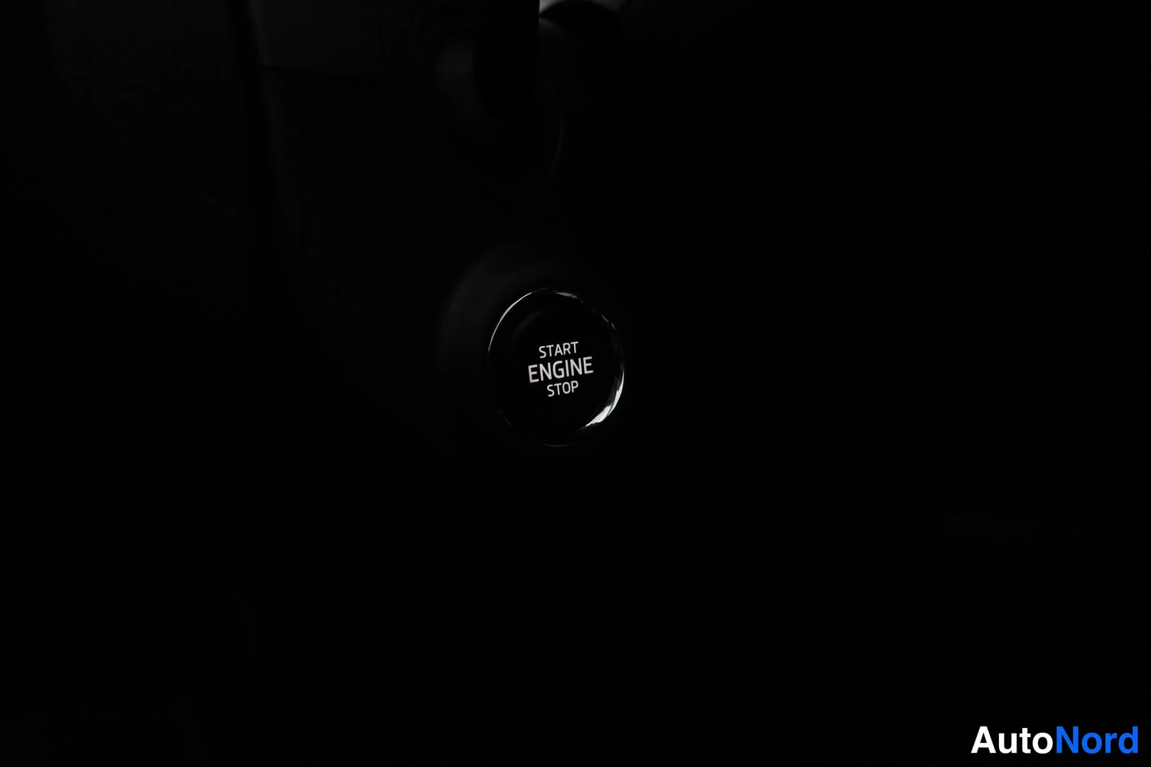 Yksityiskohta: START ENGINE STOP -painike tumman sisustuksen kohdalla, valaistu painike mustalla pohjalla.