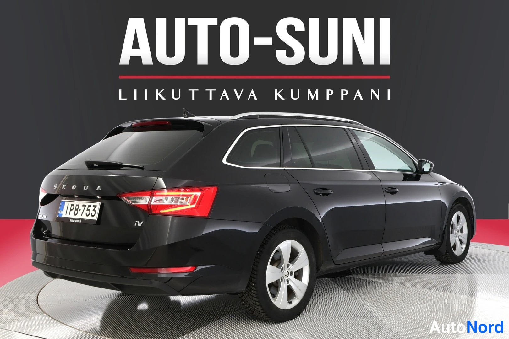 Takaviisto: Rear three-quarter view of a dark grey Skoda Superb from the rear-right angle. Visible elements include taillights with red illumination, chrome trim on rear wi