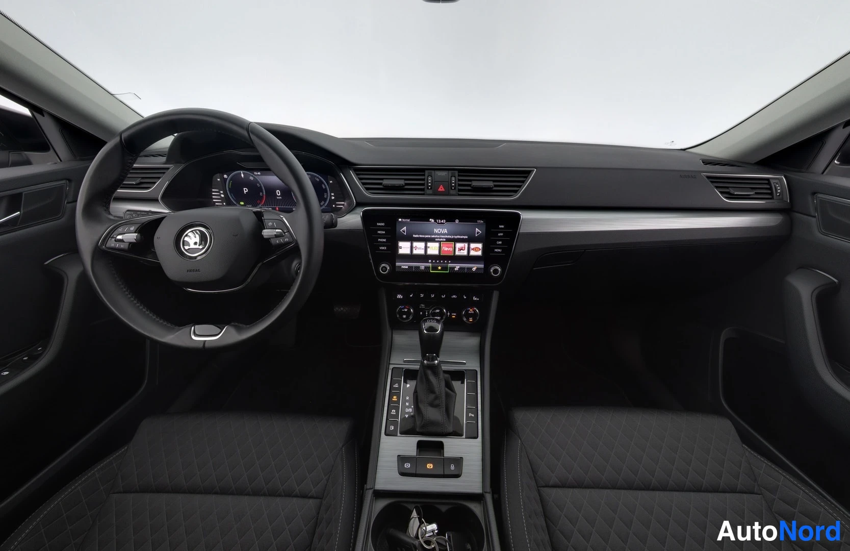 Ohjaamo: Interior dashboard shot showing the steering wheel, digital instrument cluster, central infotainment screen displaying 'NOVA', center console gear shifter, and