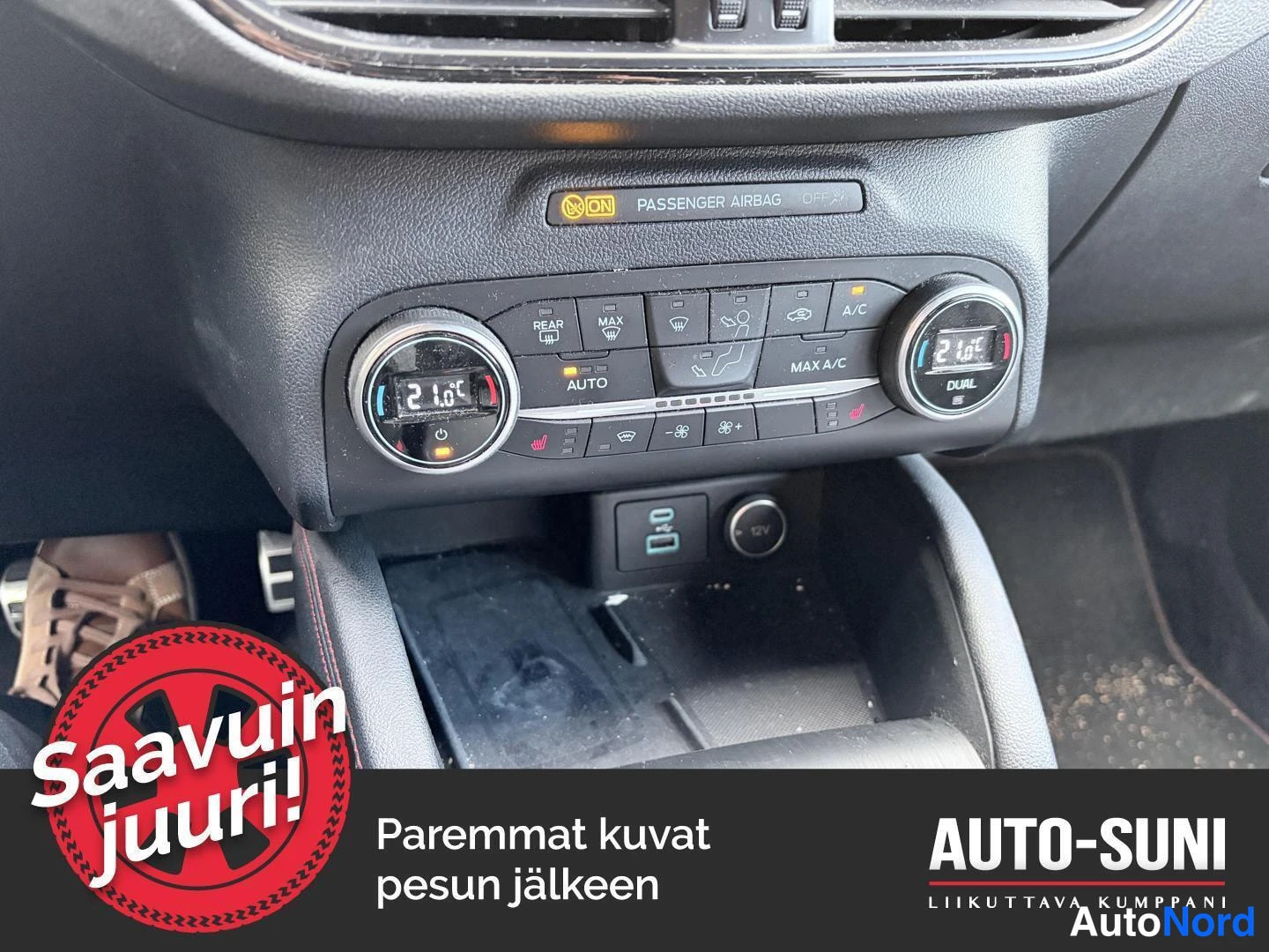 Ohjaamo: Kohdennettu kuva autotallin ilmastointiohjaimesta. Keskellä on digitaaliset näytöt lämpötiloille 21.0°C molemmilla puolilla, säätimillä ohjelmoituna AUTO. Yllä