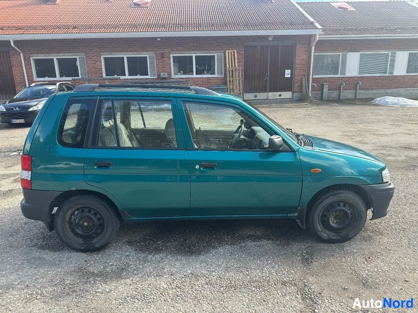 Sivulta: Vasemmalle kuvattu profiilikuvakaappaus vihreässä Mazdassa Demiossa. Autossa on kattohankaukset.