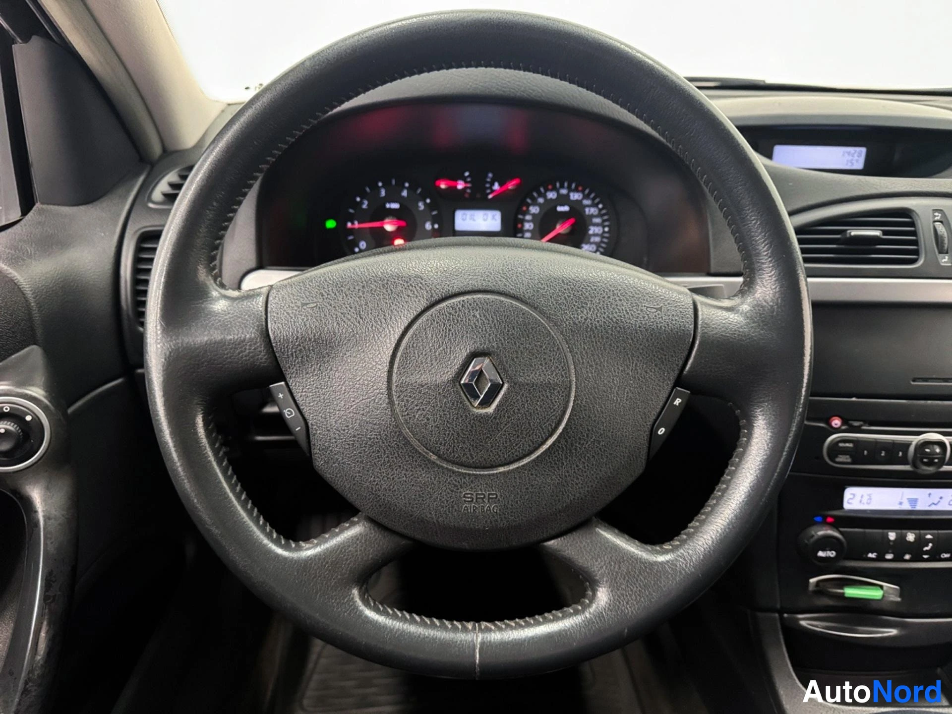 Muu: Ohjauspyörän lähikuva: Renault-logon kuvake ja merkintä 'SRP AIRBAG'. Taka-Seuraajanäyttö näkyy kojetaulussa.