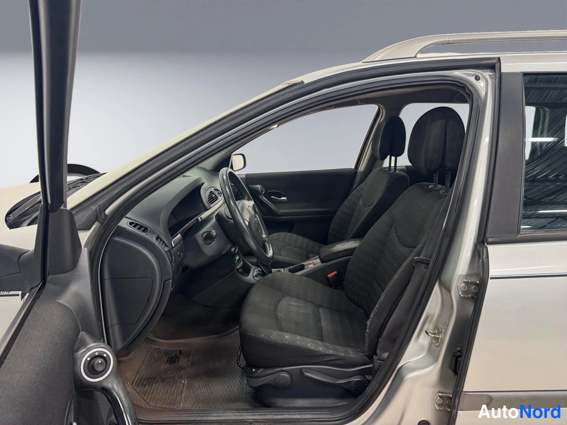 Muu: Renault Lagunan sisätila etuovista katsottuna: tummat kangasistuimet, ohjauspyörä ja kojelauta.