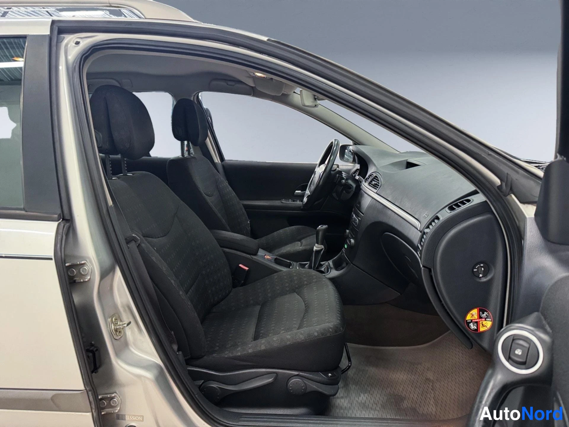 Muu: Renault Lagunan sisätila matkustajan puolen ovesta katsottuna: tummat kangasistuimet, manuaalivaihteisto ja kojelauta.