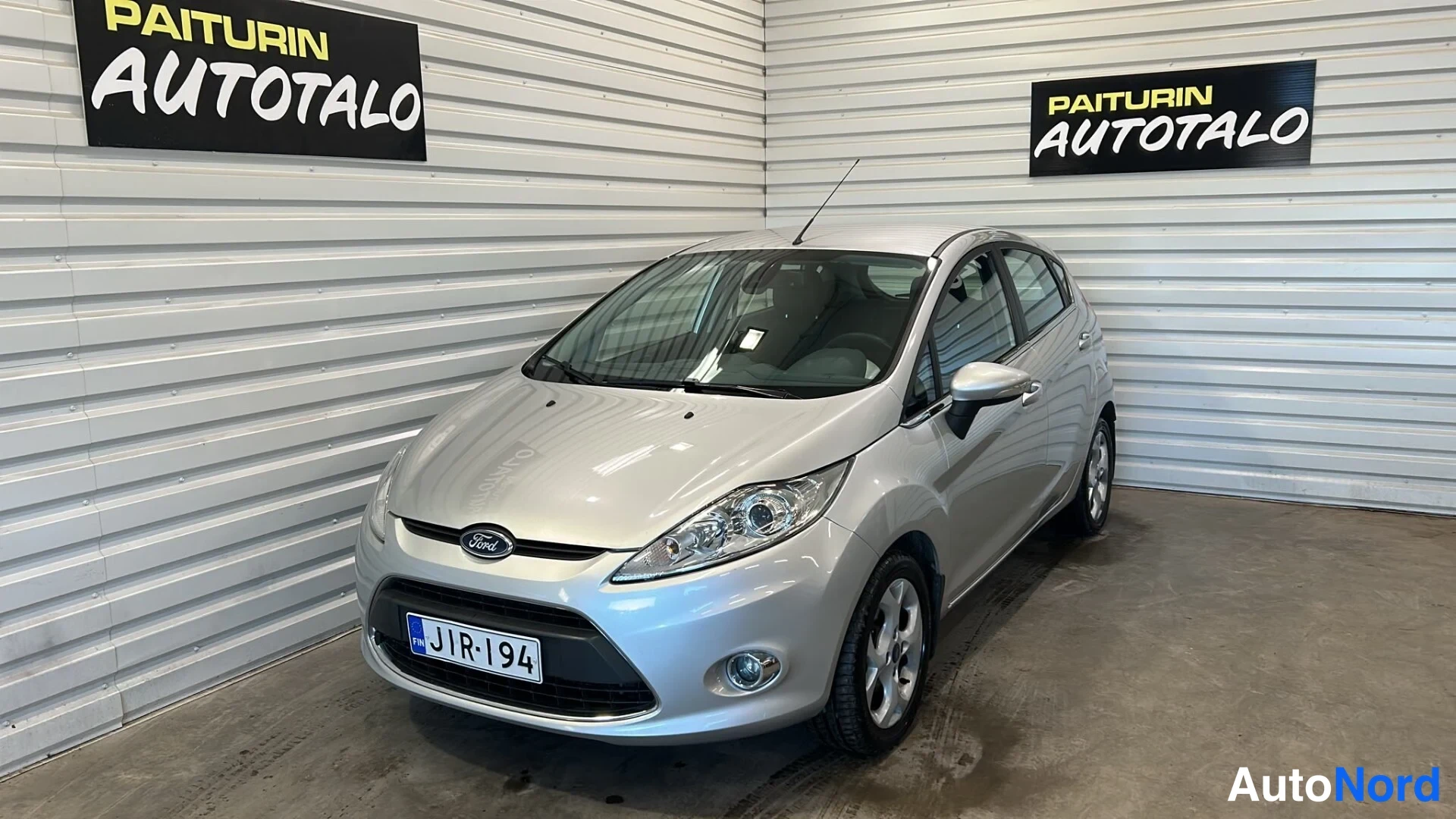 Etuviisto, nokka vasemmalle: Hopeanharmaa Ford Fiesta vasenta etuviistosta kuvattuna autotallissa, rekisterikilpi.