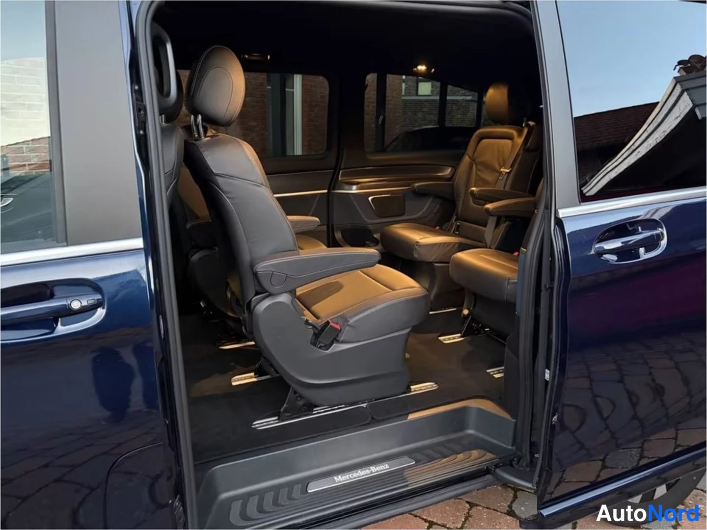 Takaistuimet: Interior view through the open side sliding door showing two individual rear captain seats with armrests on a dark carpeted floor.