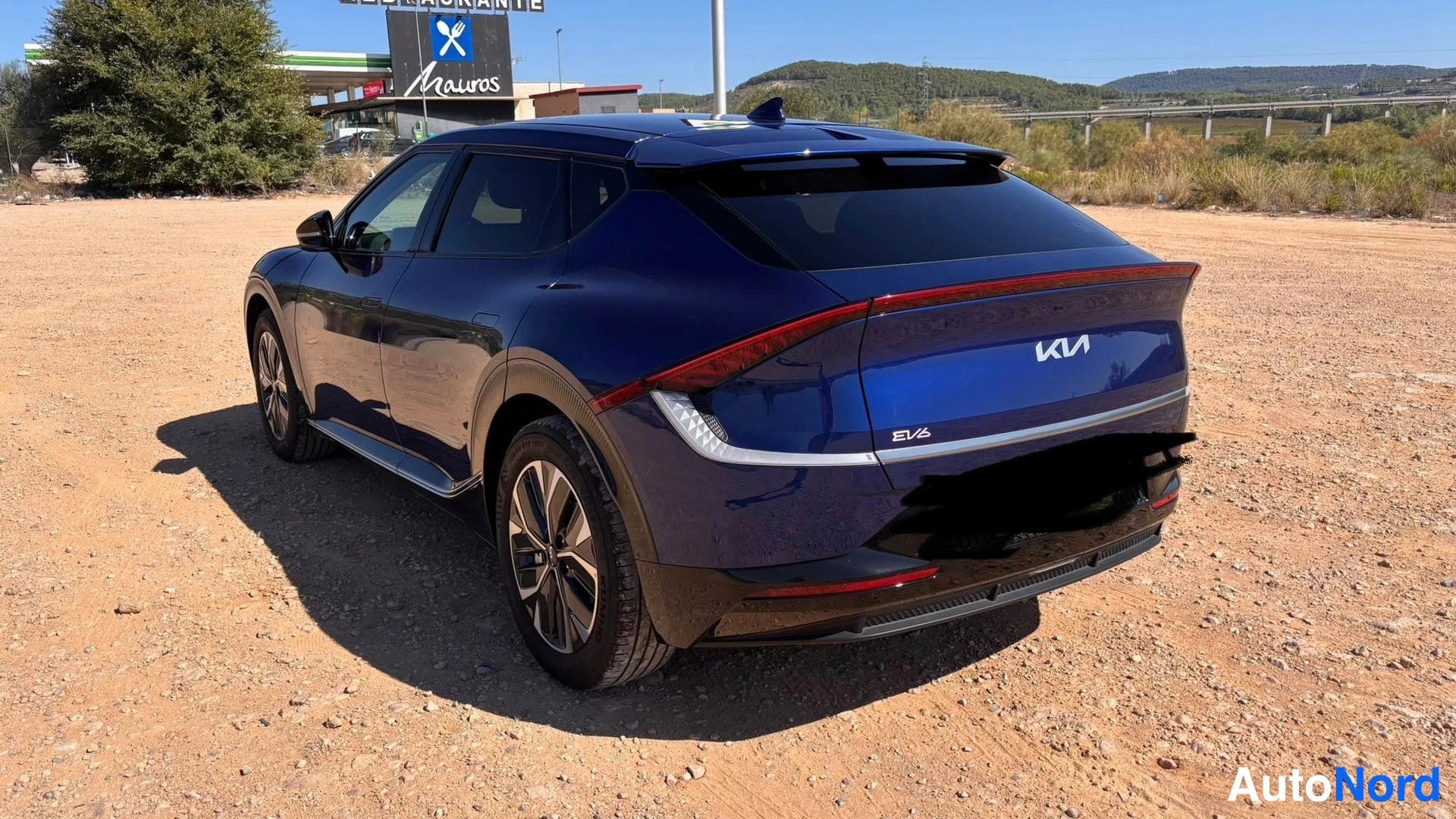 Takaviisto: Tummansininen Kia EV6 takaa kolmasosakulmasta kuvattuna hiekkaisella paikalla