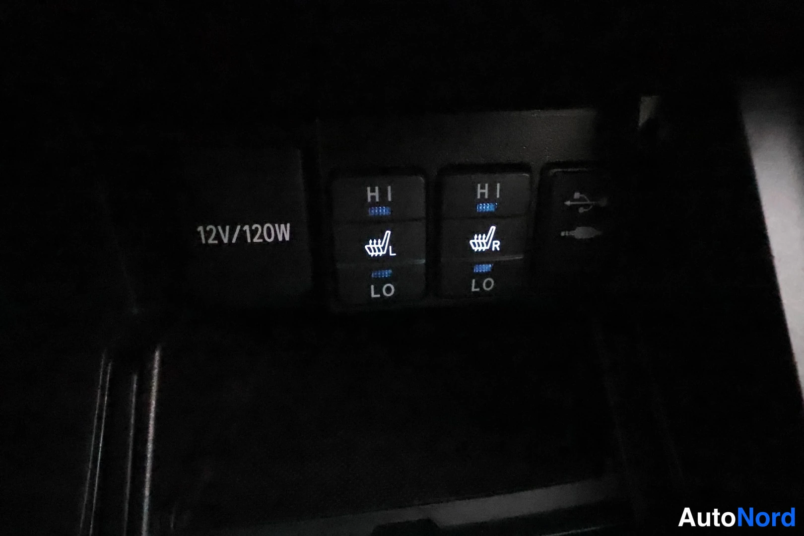 Yksityiskohta: Sisätilojen kojelaudan kytkinpaneeli: vasemman ja oikean istuimen lämmityskytkimet HI/LO-merkkauksilla, 12V/120W-pistorasian merkintä sekä USB-liittimet.