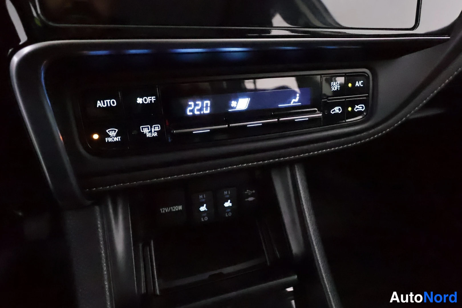 Muu: Autoetuskeulaan suunnattu lähikuva ilmastointipaneelista, jossa näkyy A/C-nappi, lämmitysnappien rivistö ja 12V/120W-pistorasia.