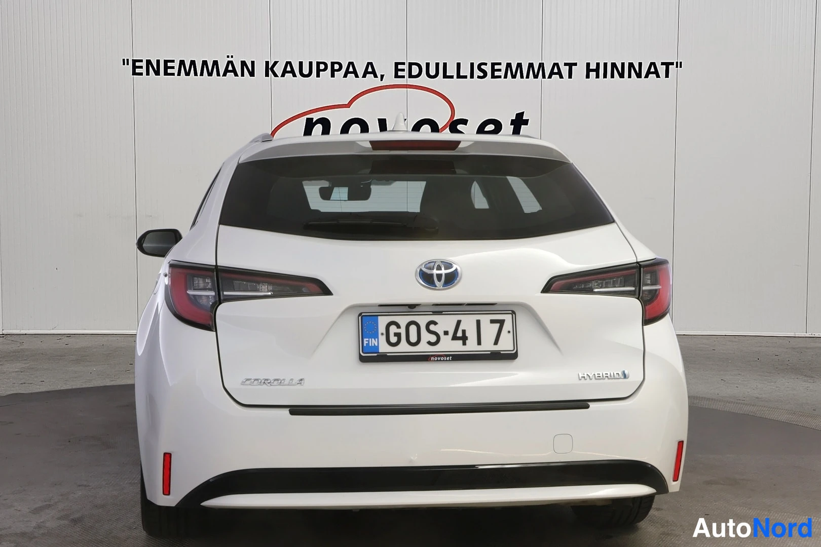 Takaa: Auto takaa: valkoinen takaosa, Toyota-merkki, rekisteritunnus ja HYBRID-tunnus.