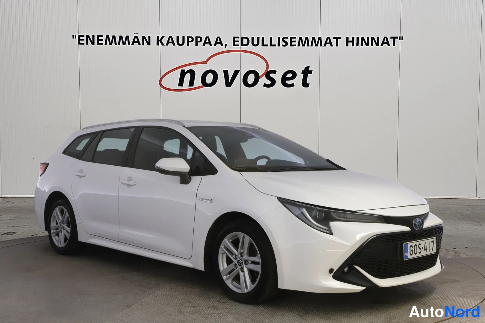Etuviisto, nokka oikealle: Valkoinen farmariauto kolmeneljäsosan etunäkymässä sisätiloissa, kylki ja keulanosa näkyvissä.