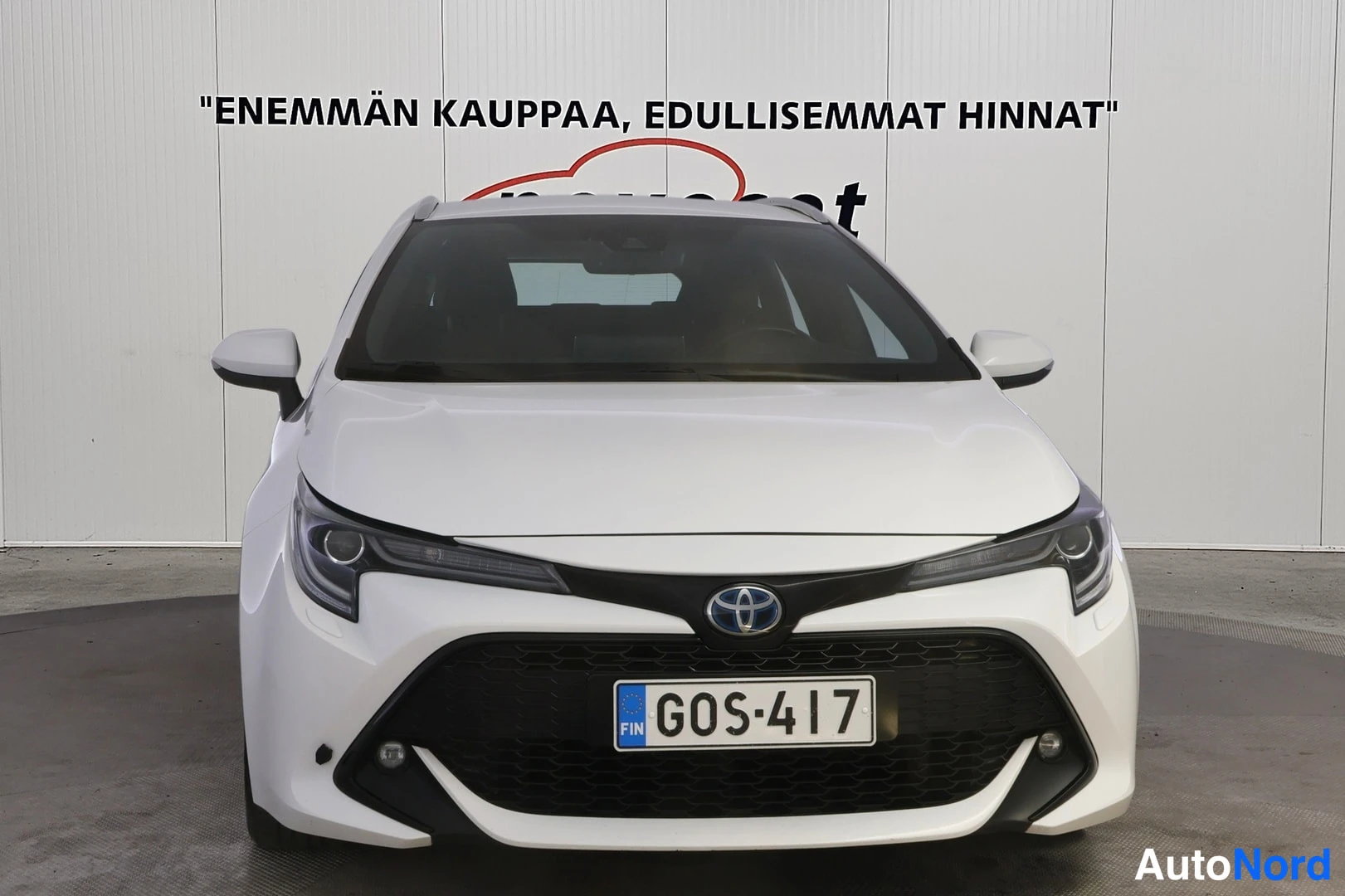 Edestä: Valkoinen farmariauto suoraan edestä päin kuvattuna, maski ja ajovalot näkyvissä.