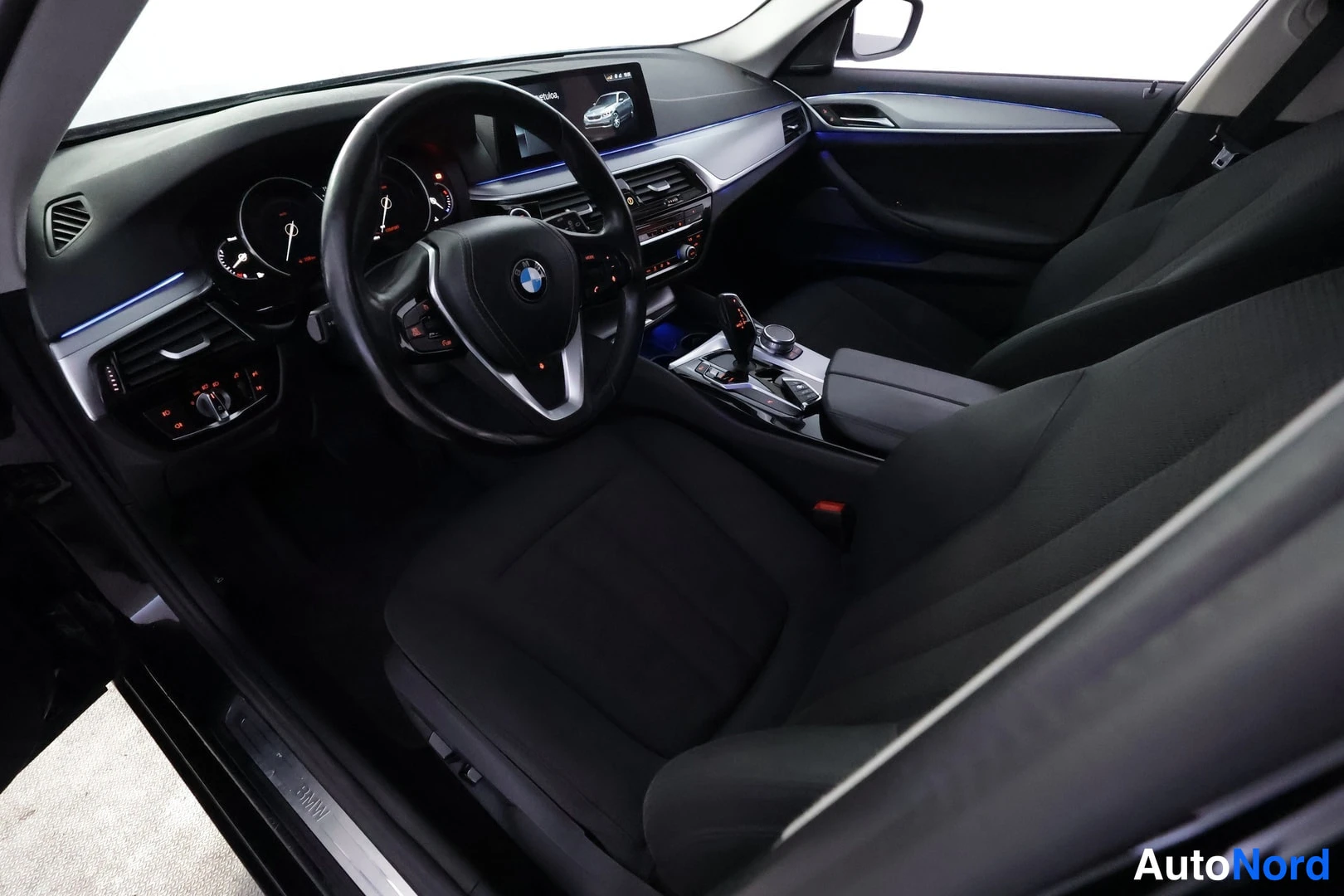 Ohjaamo: Autoon katsova kuva auton ohjaamosta näkyvissä on BMW:n logo, mittaristo, vaihteet ja valkoiset istuimet.