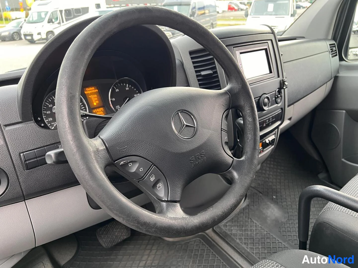 Etuistuimet: Lähikuva ohjauspyörästä ja mittaristosta. Ohjauspyörän keskellä on Mercedes-logo ja se on varustettu painikkeilla. Mittariston takana on kellotaulu.