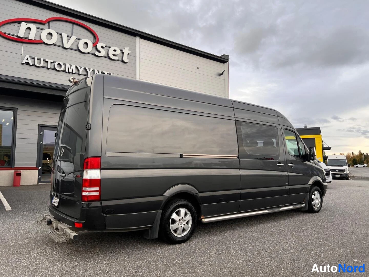 Takaviisto: Tummanharmaa Mercedes-Benz Sprinter kuvattuna taka-oikealta kolmannesvinkkelistä. Takaovi, takavalot ja vetolaitteisto ovat selvästi nähtävissä. Auto seisoo ulk