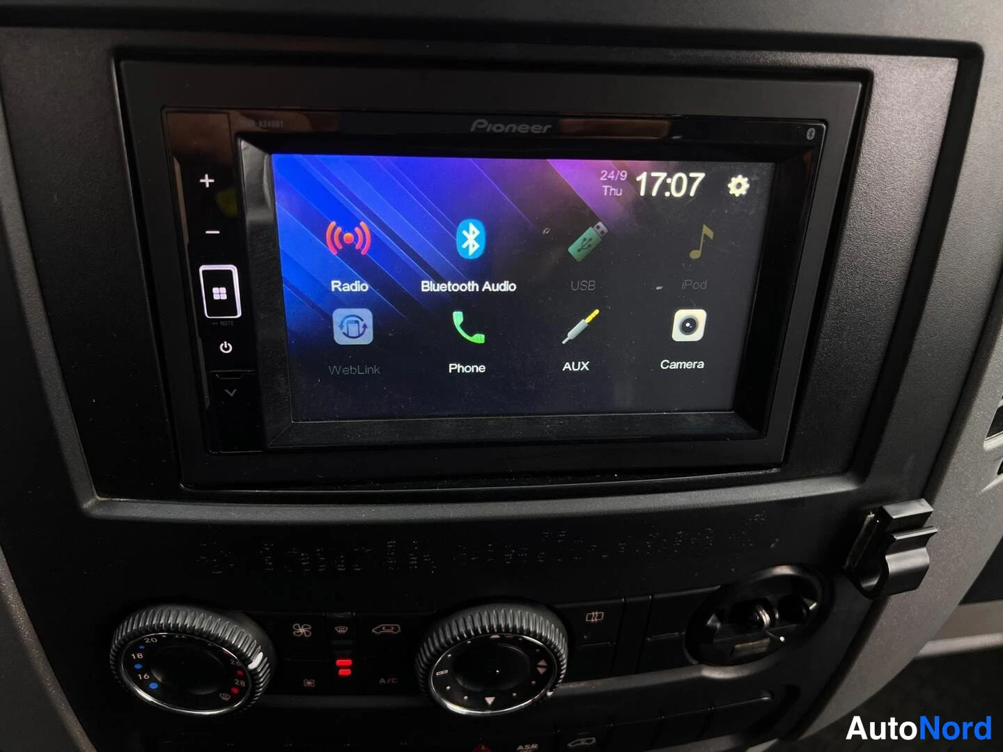 Muu: Sisäkuva kojelaudasta: Pioneer-radiolla kosketusnäyttö, jossa valikot Radio, Bluetooth Audio, USB, iPod, WebLink, Phone, AUX ja Camera ja kello 17:07; alla ilma