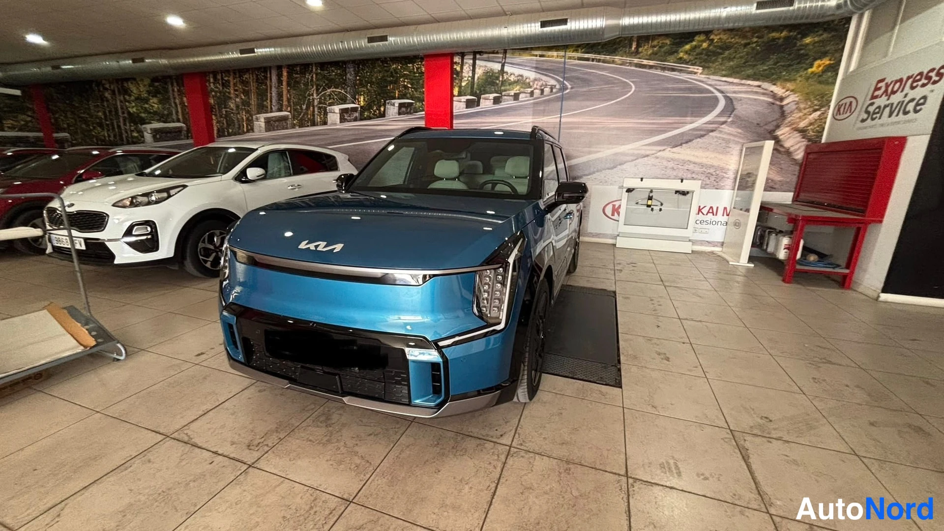 Etuviisto, nokka oikealle: Kuvan kulmasta nähtynä tumansininen Kia-EV9: n edestön puolikas oikealta puolelta on esillä showroomissa.