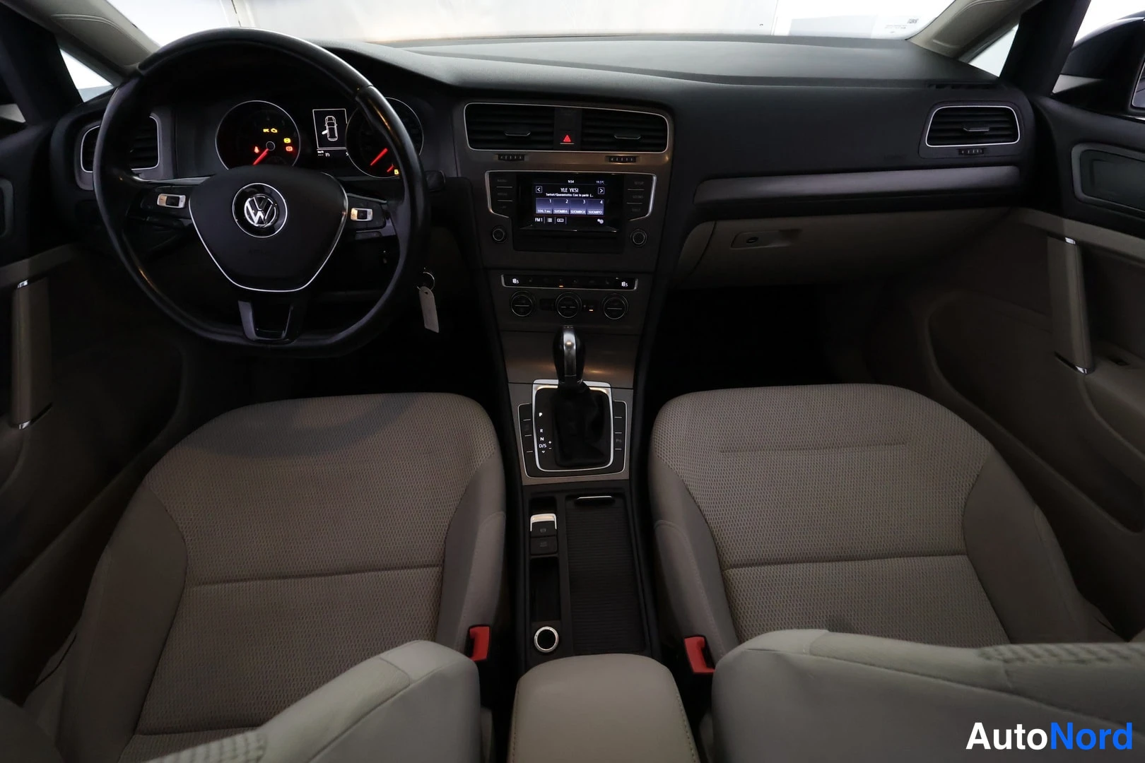 Sivulta: Näkymä ohjaamoon takaapäin: Volkswagen-ohjauspyörä, mittaristo, kosketusnäytöllinen radiopaneeli, automaattivaihteen valitsin (P R N D -merkinnät) ja kaksi vaal