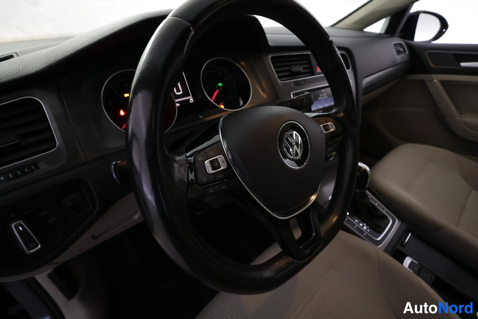 Muu: Ohjaamon sisäkuva: Volkswagen-ohjauspyörä, mittaristo ja tumma kojelauta, beiset istuimet ja vaihtajan keila näkyvillä.
