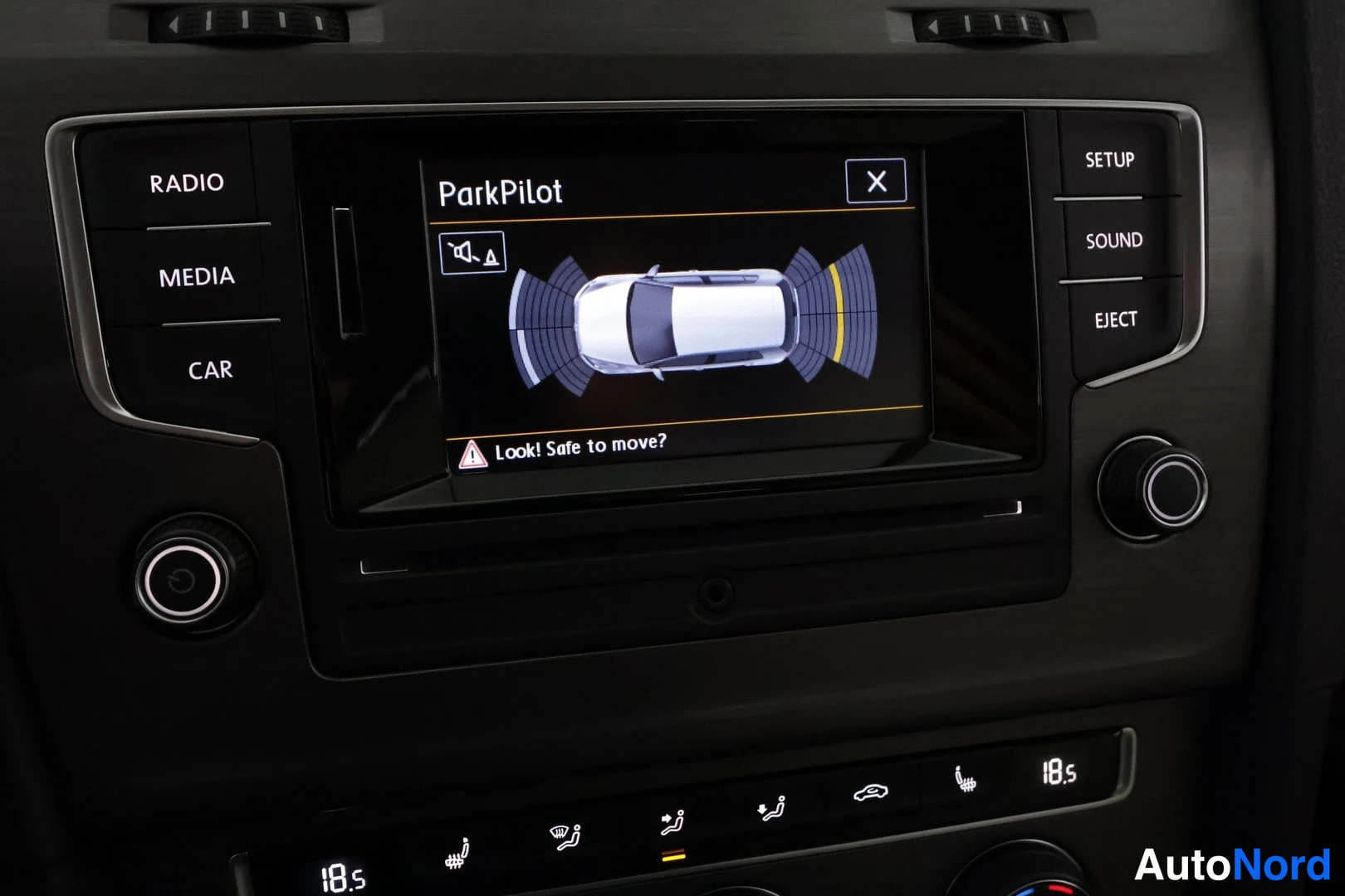 Muu: Sisäkuva kojelaudan kosketusnäytöstä: ParkPilot-ohjaustieto, jossa auton kuva ja pysäköintianturin kaartit. Näytön teksti ParkPilot ja Look! Safe to move?