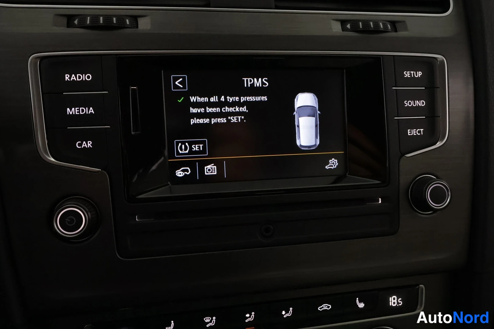 Muu: Keskikonsolin infotainment-näyttö lähikuva, näytöllä TPMS eli rengaspainevalvontajärjestelmän asetusnäkymä ohjeineen ja valkoisen auton piktogrammilla.