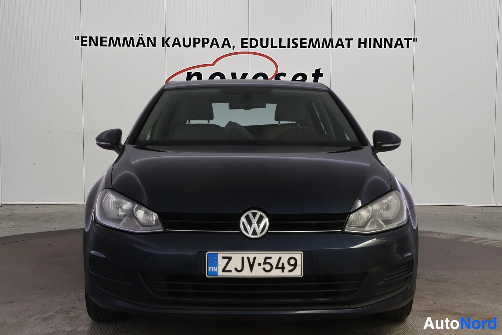 Edestä: Frontal view of dark blue hatchback with grille, VW emblem and headlamps visible.