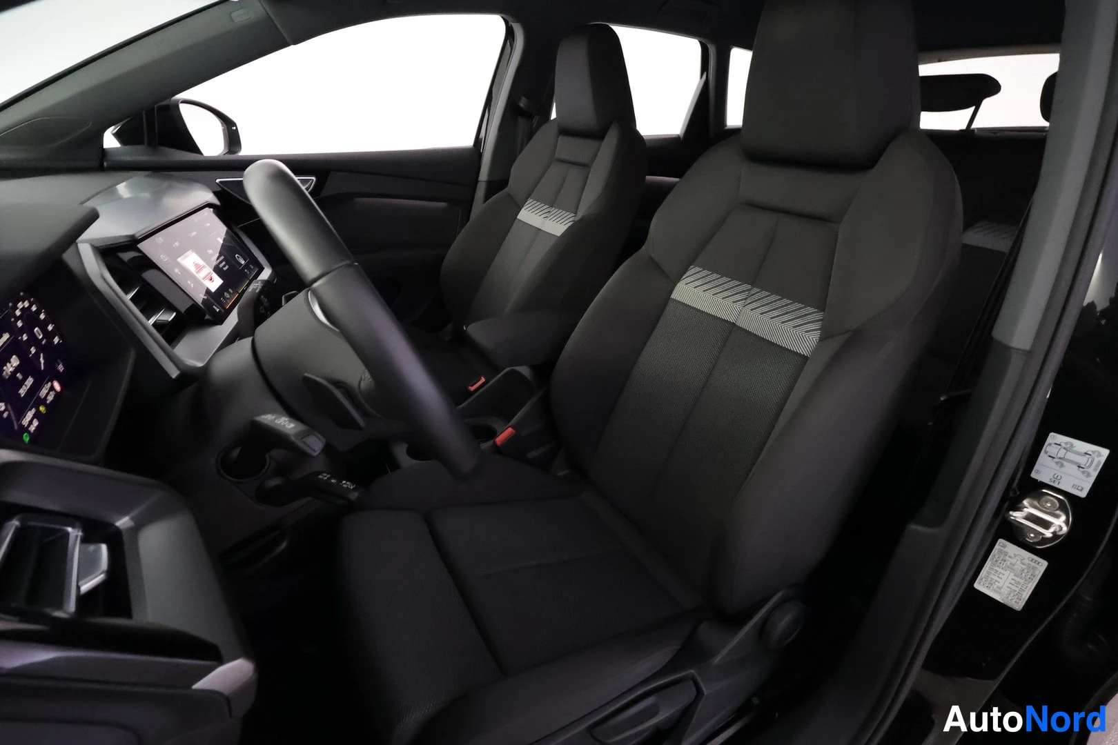 Edestä: Audi Q4:n sisätilat: ohjaamo paljailla kankaanistuimilla, ritiläkuosikankaat, kosketusnäyttö ja digitaalinen mittaristo näkyvät.