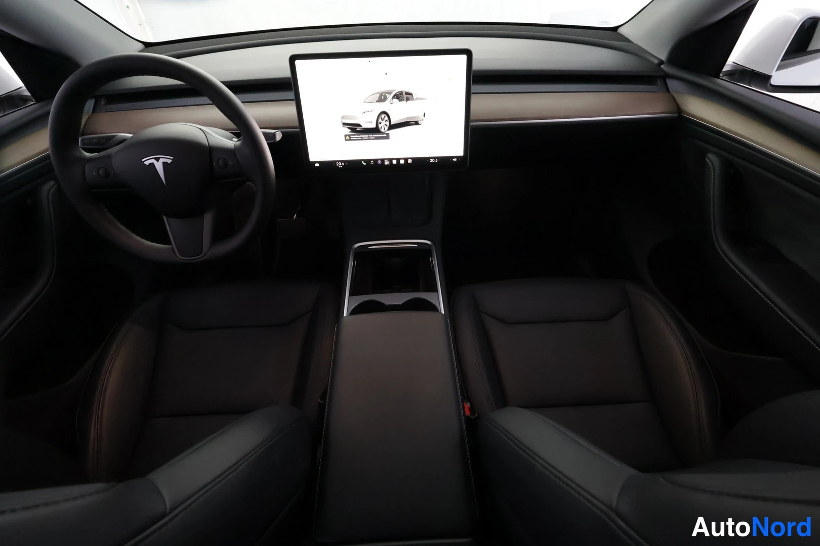 Muu: Tesla Model Y:n sisätilat, mustat etuistuimet ja ohjauspyörä sekä keskikonsolin suuri kosketusnäyttö, joka näyttää valkoisen auton kuvaa.