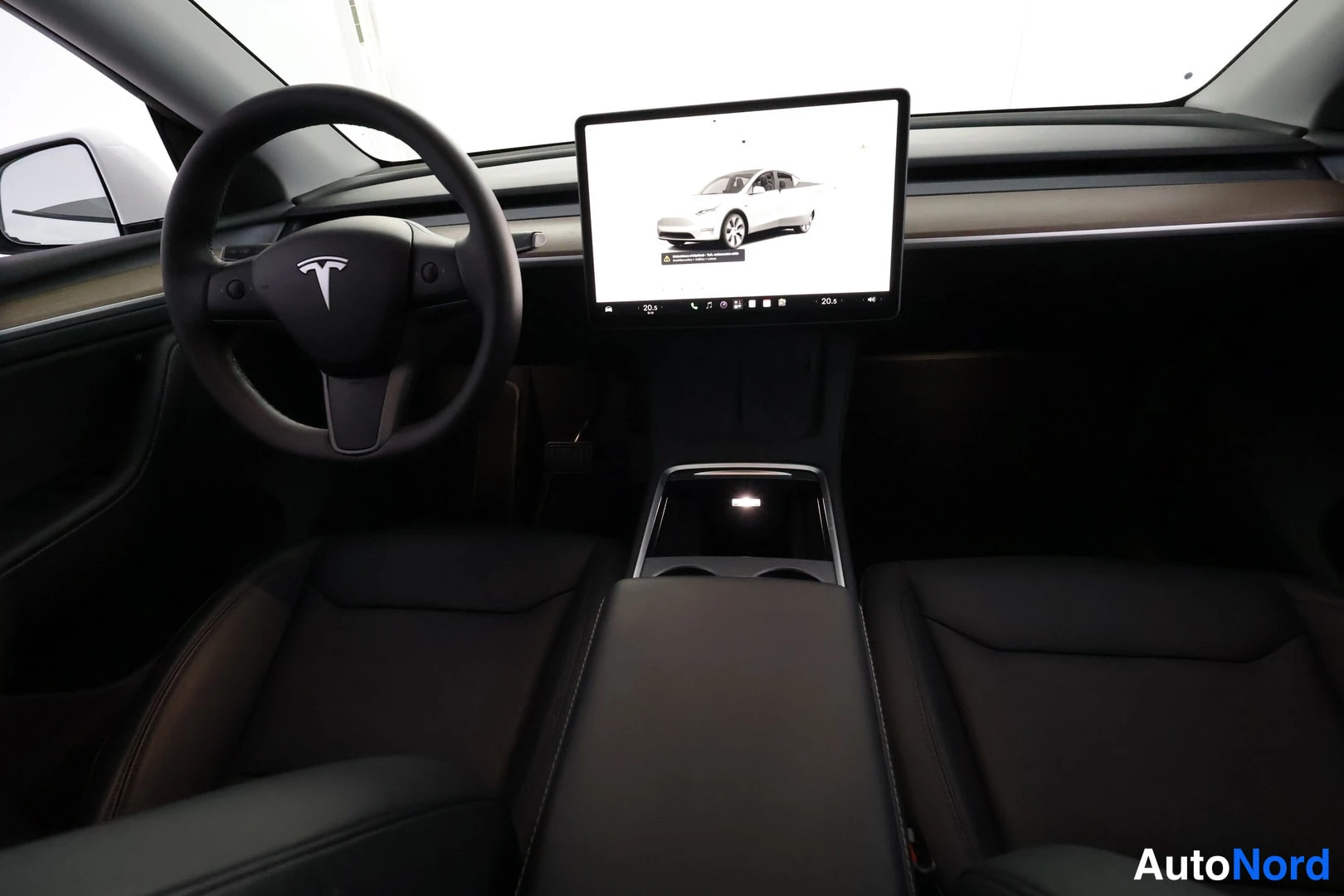 Muu: Tesla Model Y:n ohjaamo lähikuva: musta ohjauspyörä Tesla-logolla, puolella avattava lasikatto ja keskikonsolin kosketusnäyttö, jossa näkyy valkoinen auto.