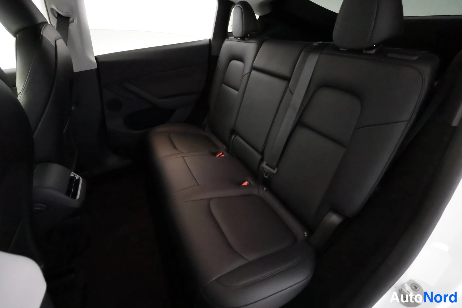 Muu: Sisäkuva auton takaistuimesta: musta penkki, turvavyöt ja punaiset isofix-merkinnät, edessä etuistuinten selkänojat.