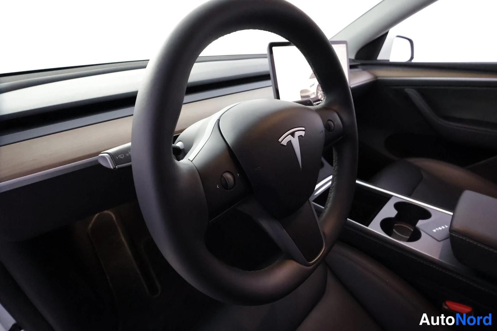Muu: Henkilöauton sisätila: Tesla-merkkinen ohjauspyörä, kosketusnäyttö kojelaudassa ja tummat penkit.